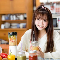 台所でスムージーを飲む女性、ミキサーと新鮮な野菜と果実の写真